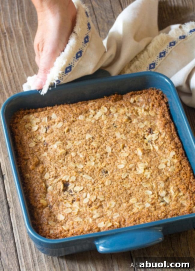 A full pan of freshly baked oat bars in a blue baking dish, golden brown and puffed, cooling on a wire rack.