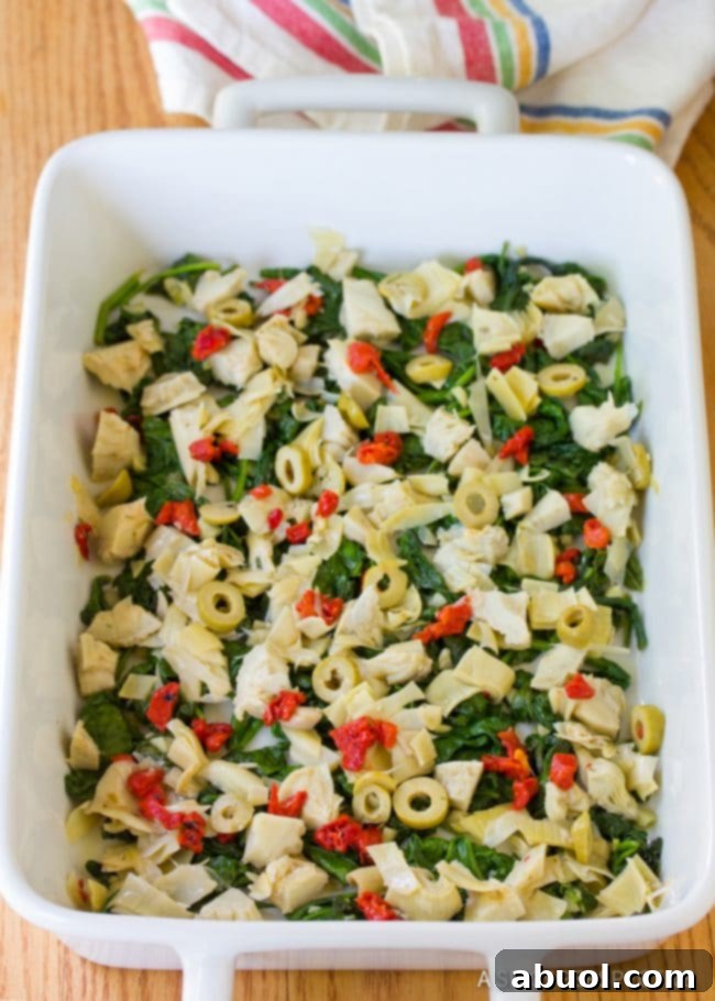 Casserole dish with spinach and artichoke salad layered neatly at the bottom.