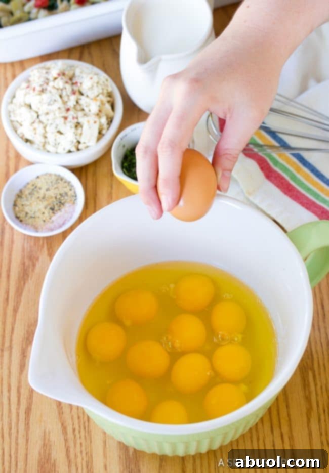 A hand cracking an egg into a white bowl, ready to be whisked for the casserole.