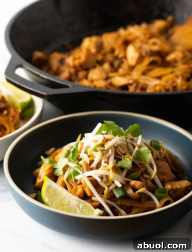 Delicious Chicken Pad Thai served in a black bowl, with a wok visible in the background, hinting at its fresh preparation.