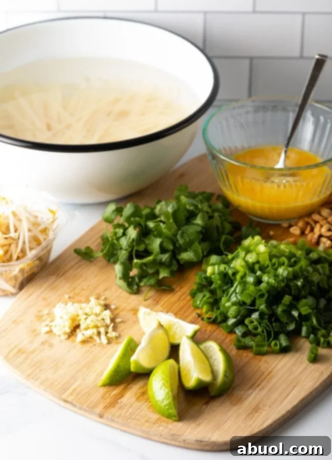 A vibrant display of Pad Thai ingredients on a wooden cutting board, including piles of minced garlic, fresh lime wedges, chopped green onions, fragrant cilantro, and a bowl of whisked raw eggs, highlighting the fresh prep.