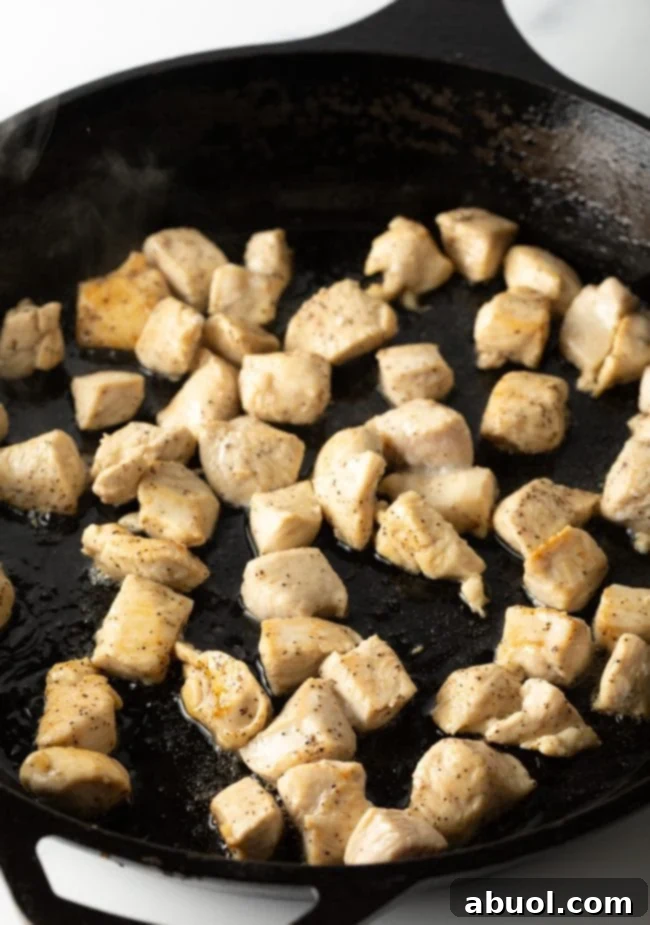 Close-up of seasoned chicken pieces sizzling and cooking in a large, deep skillet or wok over medium-high heat, turning golden brown and tender.