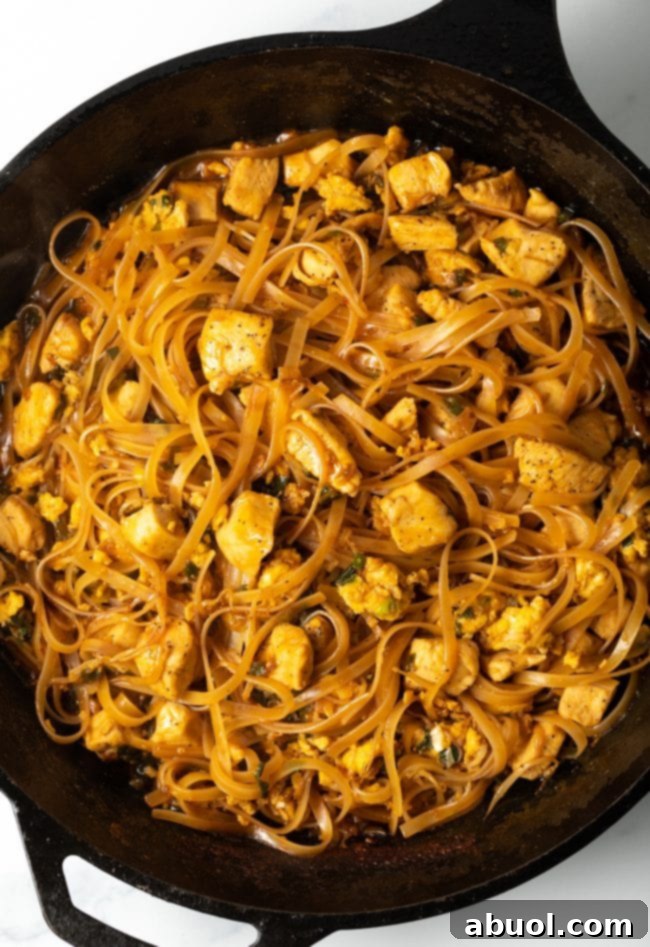 A mouth-watering top-down view of freshly made Pad Thai chicken with noodles, artfully arranged in a rustic cast iron skillet, ready to be served.
