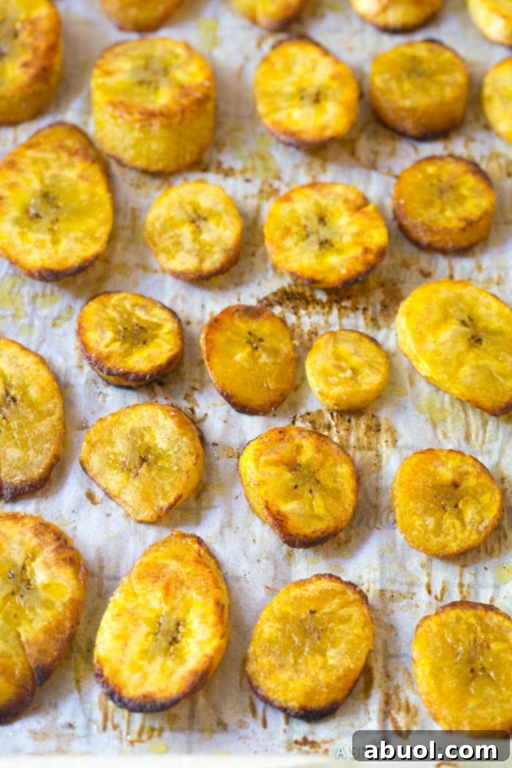 Diagonal slices of ripe plantains, coated with olive oil and a generous sprinkle of salt, arranged neatly on a parchment-lined baking sheet before baking.