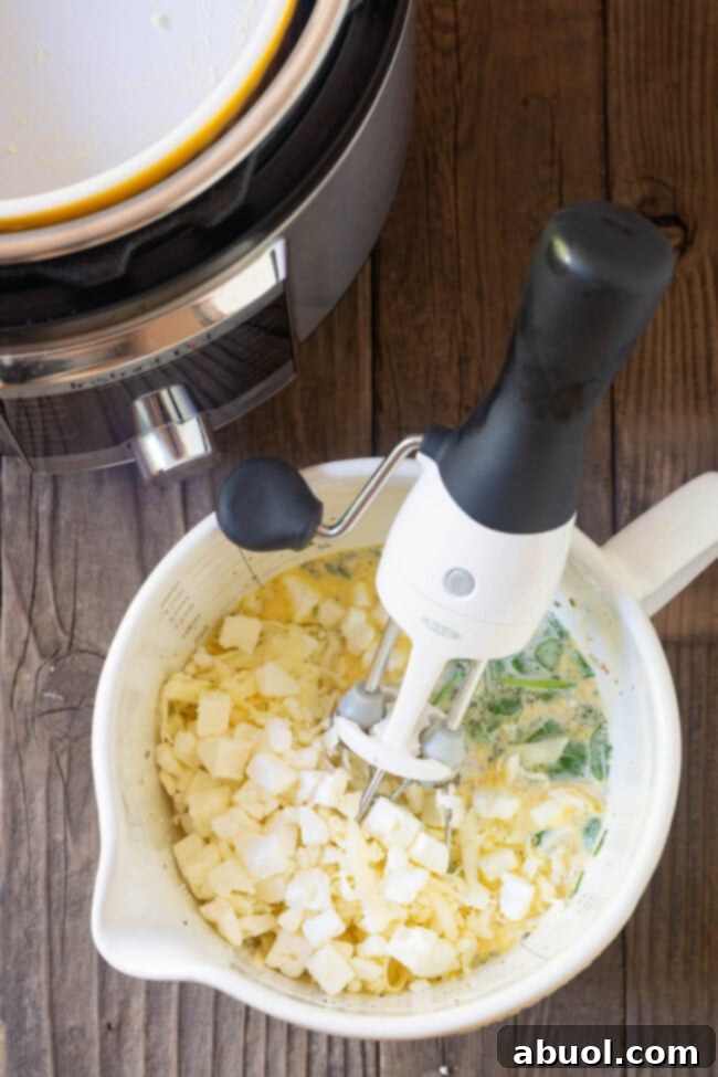 A mixing bowl filled with quiche ingredients, including eggs, cream, spinach, and cheese, being whisked with an electric mixer.