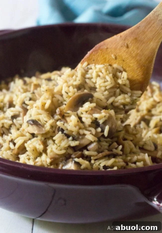 Freshly cooked mushroom rice pilaf in a pan, being gently stirred with a wooden spoon, showcasing its fluffy texture and inviting aroma.