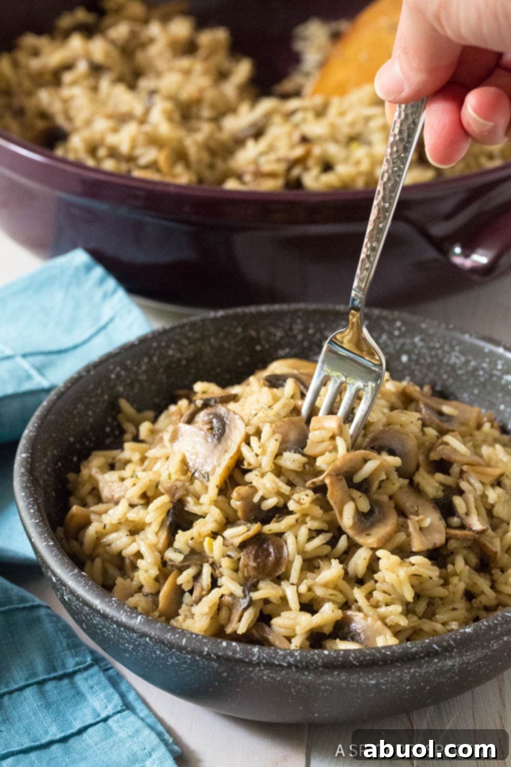 A serving of Mushroom Rice Pilaf in a black bowl, with a fork poised to take a bite, highlighting its tempting texture and the promise of rich flavor.