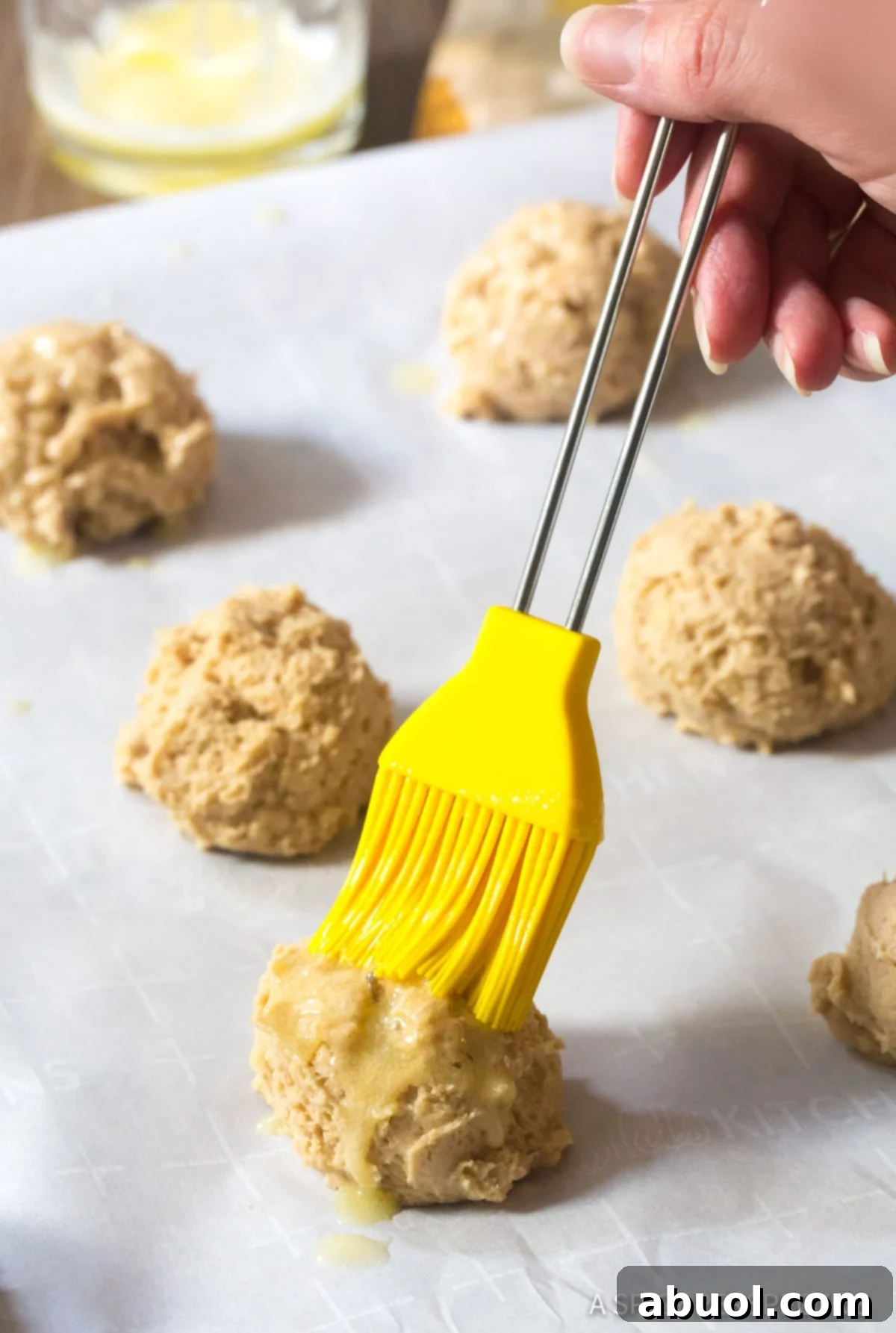 Brushing unbaked Cinnamon Biscuits with melted butter before baking for enhanced flavor and golden crust