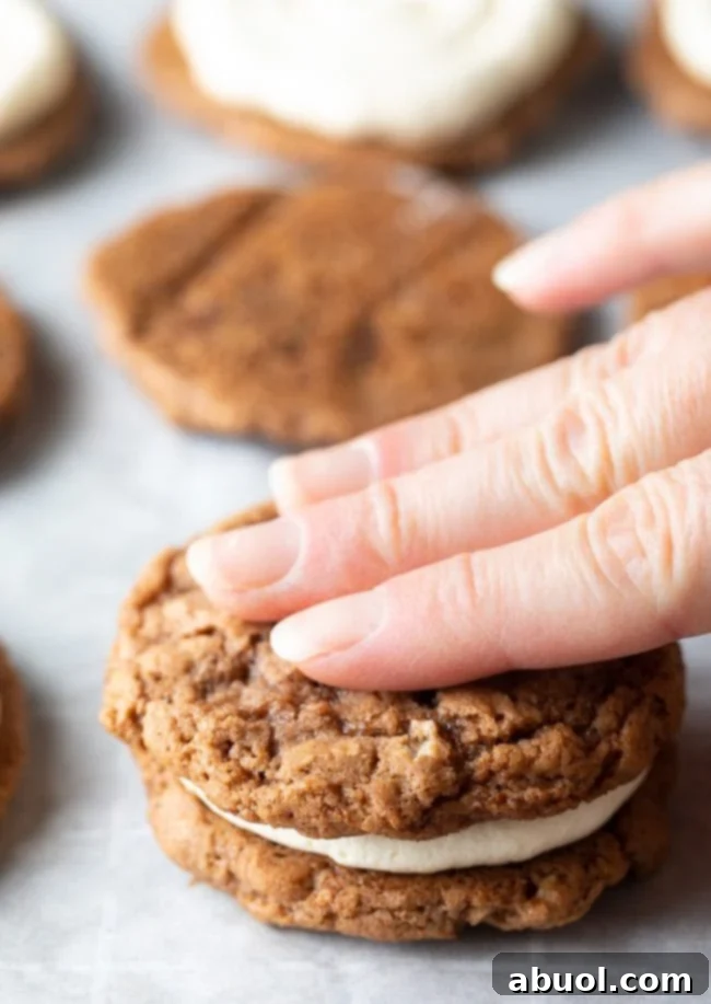 Hand pressing top layer of oatmeal cookie over cream filling. 