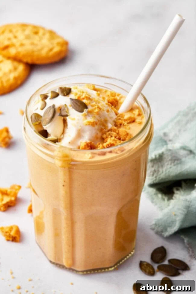 A delicious pumpkin pie milkshake topped with whipped cream, a sprinkle of pepitas, and crushed gingersnap cookies. It’s served in a tall glass with a festive striped straw, embodying the spirit of autumn.