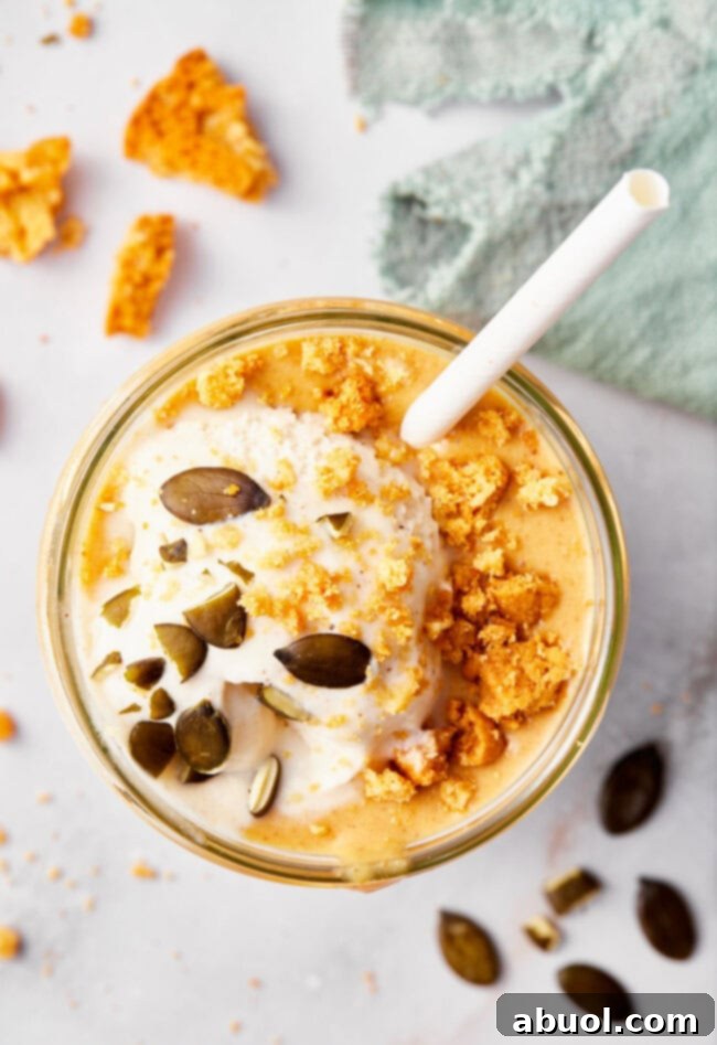 An overhead shot of a beautifully garnished pumpkin pie milkshake, featuring whipped cream, crushed gingersnaps, and a sprinkle of spices, presented invitingly.