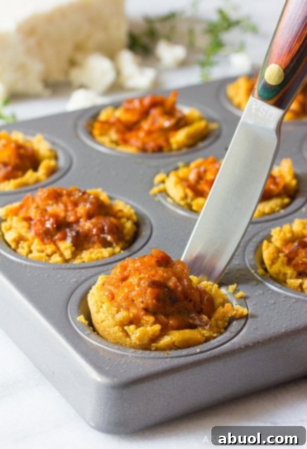 Freshly baked mini tamales being gently removed from a baking sheet using a small utensil.