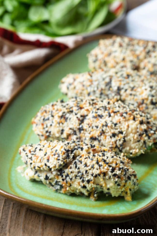 Five perfectly rolled chicken breasts coated in everything bagel seasoning, arranged on a vibrant green plate, ready to be enjoyed.