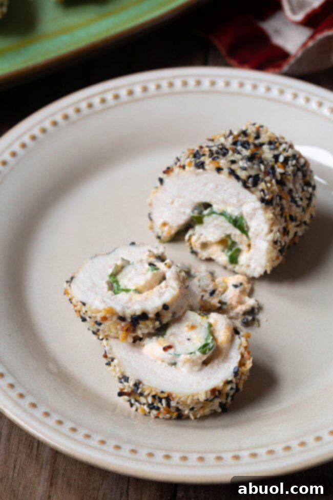 A beautifully sliced chicken breast roll-up, revealing the creamy cream cheese and vibrant spinach filling, coated in savory everything bagel seasoning.