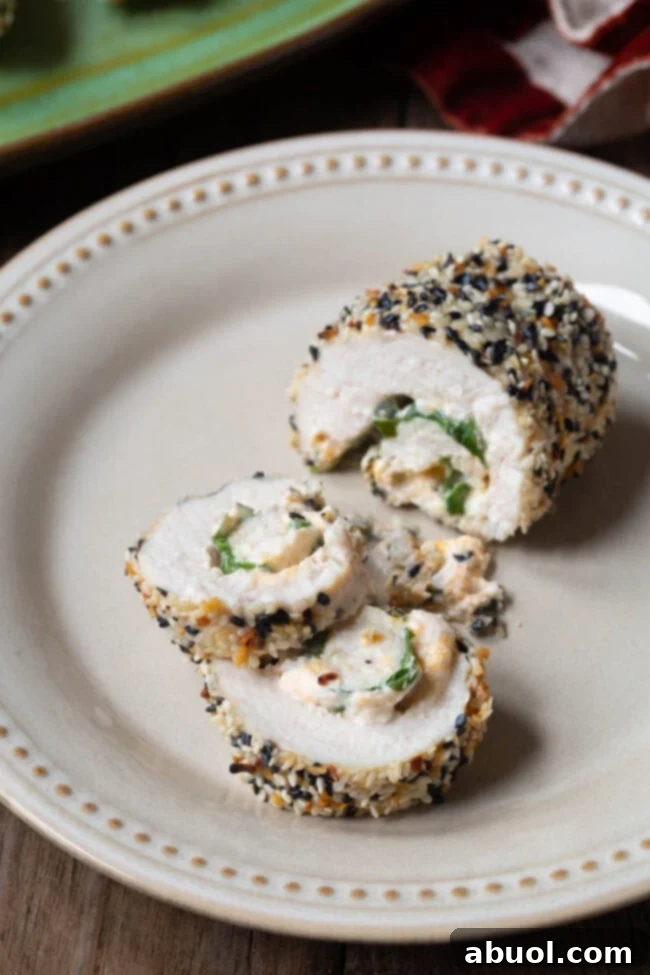 A perfectly cooked and sliced chicken breast roll-up, showing its rich, creamy filling of cream cheese and spinach, surrounded by a crispy everything bagel seasoning crust.