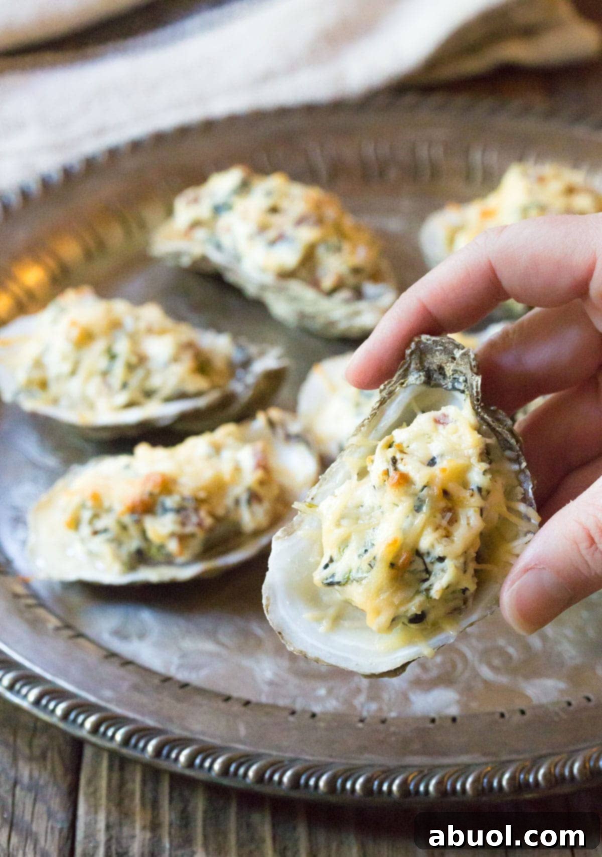Close-up of a perfectly baked oyster, filled with melted three-cheese and bacon, held in hand ready to be enjoyed.