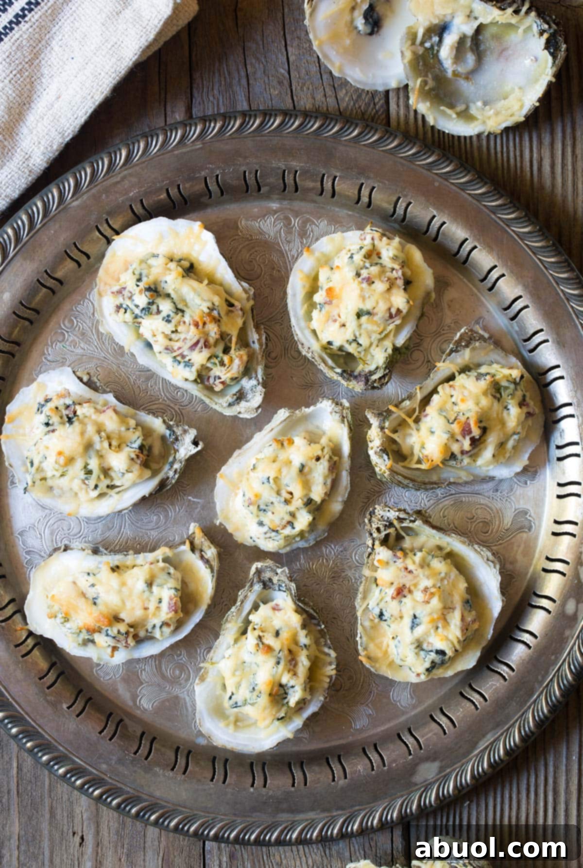 Overhead view of a baking tray filled with cheesy baked oysters in the half shell, garnished and ready for serving.