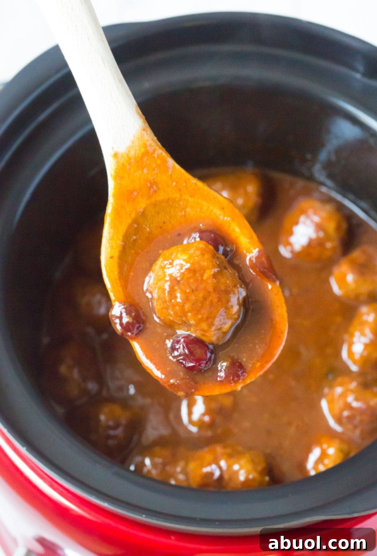 Top view of a wooden spoon holding a single cocktail meatball with some of the cranberry BBQ sauce