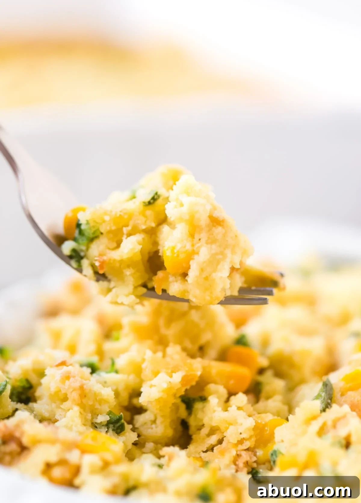 Our Corn Pudding Recipe. A close-up side view of a fork gently picking up a delectable bite of this tender corn soufflé, highlighting its soft texture.