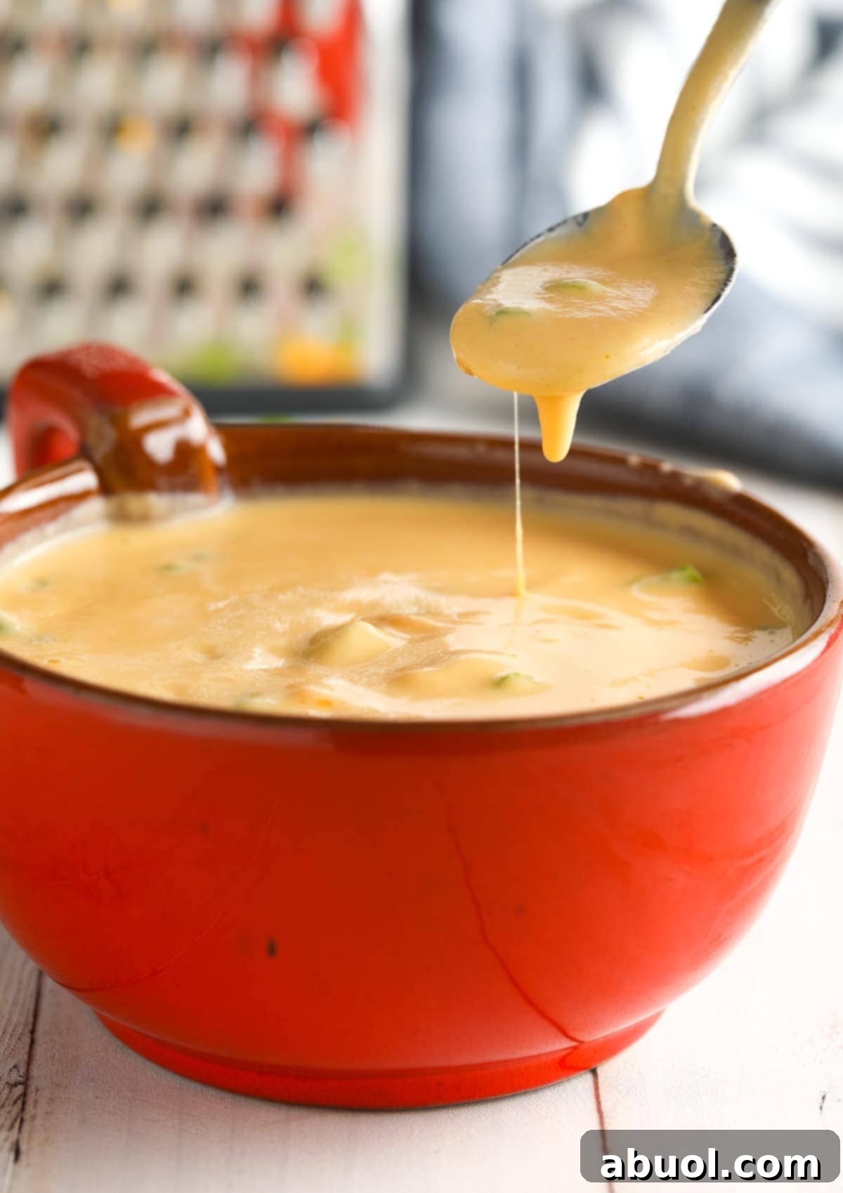 Lifting spoonful of Cauliflower Cheese Soup up out of red bowl.