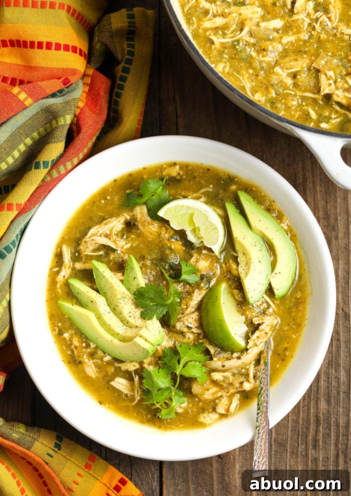 Top view of this bright green chicken chili verde in a bowl topped with some creamy avocado slices and fresh cilantro. A perfect low-carb and Whole30 meal.