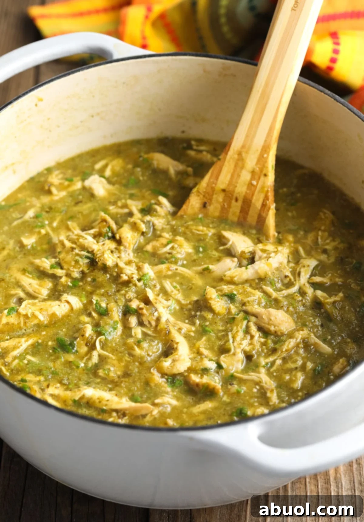 Side view of a wooden spoon stirring the final chicken chili soup in a pot, highlighting the rich green color and hearty texture of the prepared dish.
