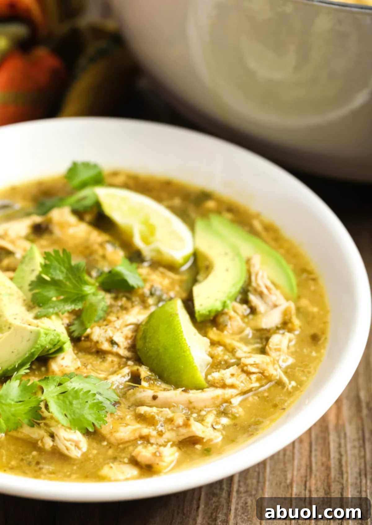Side view of a bowl of Paleo Chicken Chili Verde, garnished with fresh avocado slices and lime wedges, emphasizing its vibrant colors and fresh appeal.