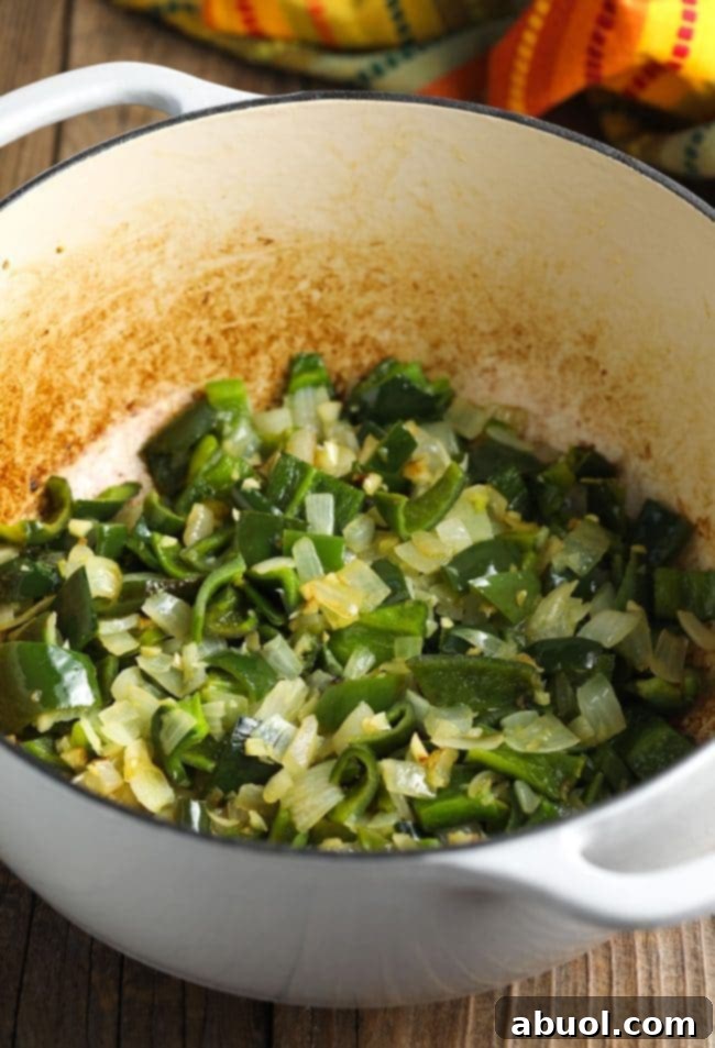 Fresh poblano and jalapeno peppers, onions, and garlic being sautéed in a pot, releasing their aromatic flavors.