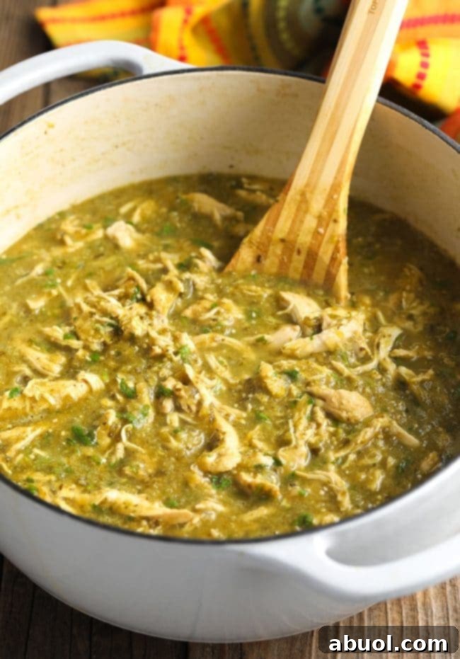 A wooden spoon combining all of the vibrant ingredients in the pot, showcasing the rich texture of the finished chicken chili verde.