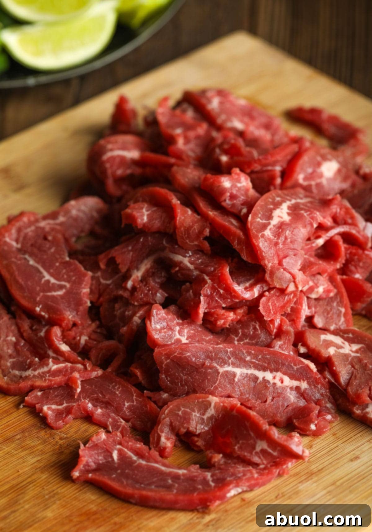 Thinly sliced raw flank steak fanned out on a wooden cutting board, ready to be added to the pho soup.