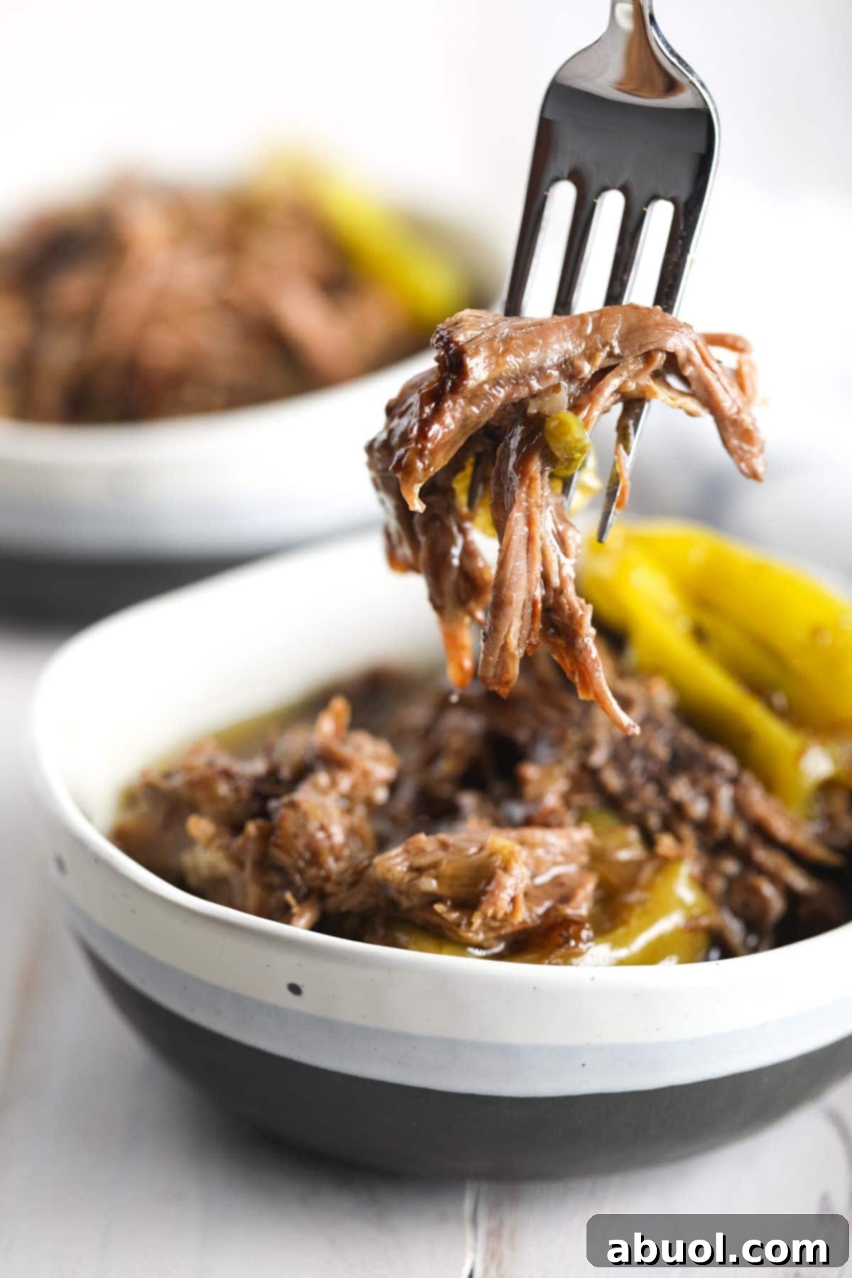 Shredded Italian beef in a bowl with a fork taking a bite or shredded beef. 