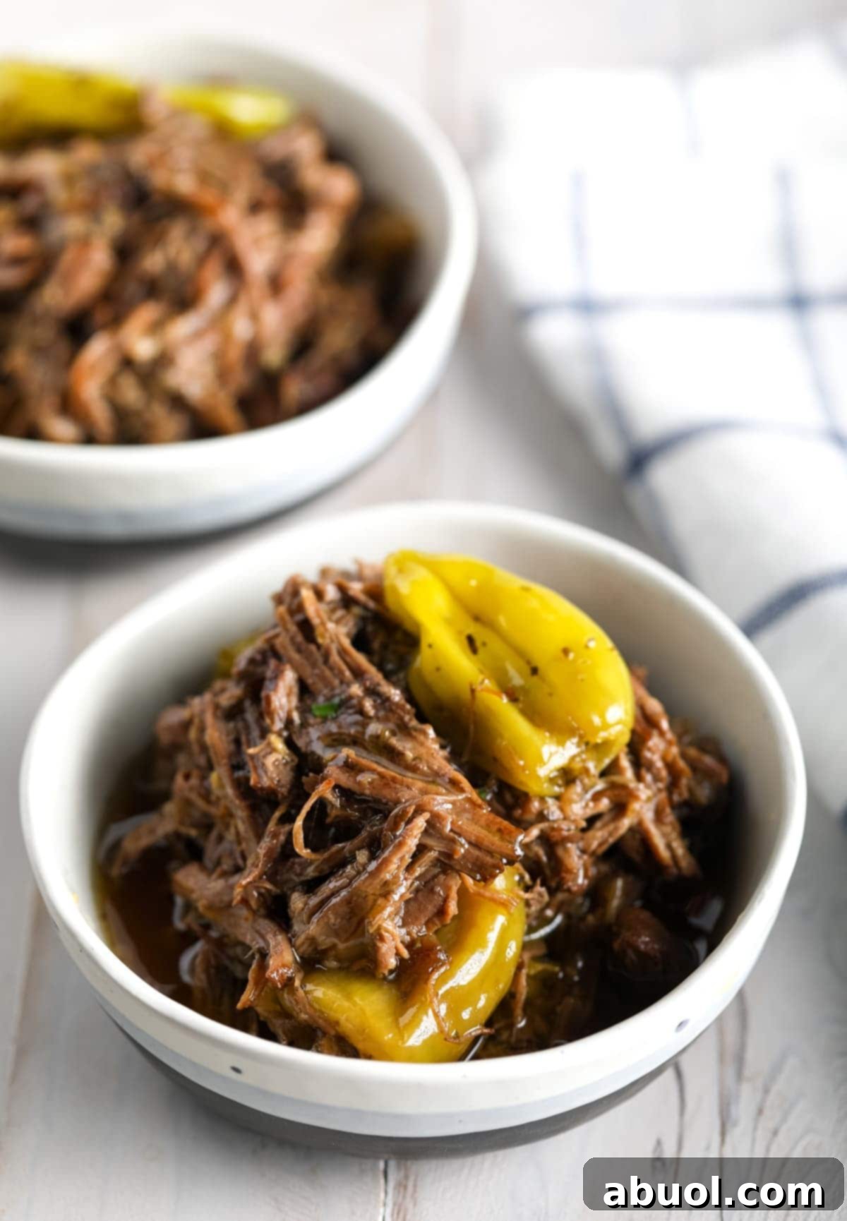 Two white bowls with Italian beef in them with pepperoncini peppers. 