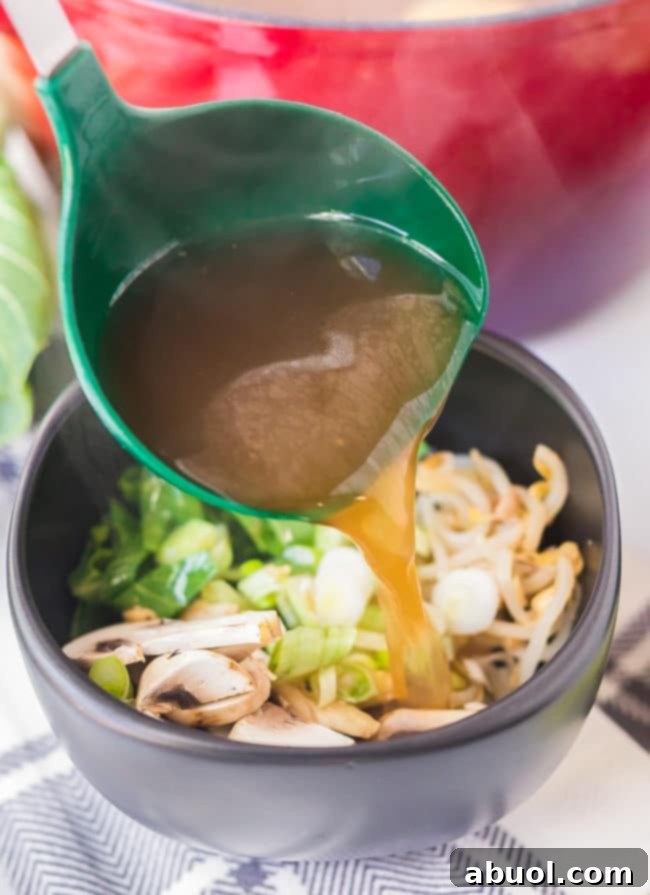 A stream of rich, savory broth being poured from a ladle over a bowl filled with an assortment of crisp, fresh vegetables, ready for the hot pot.