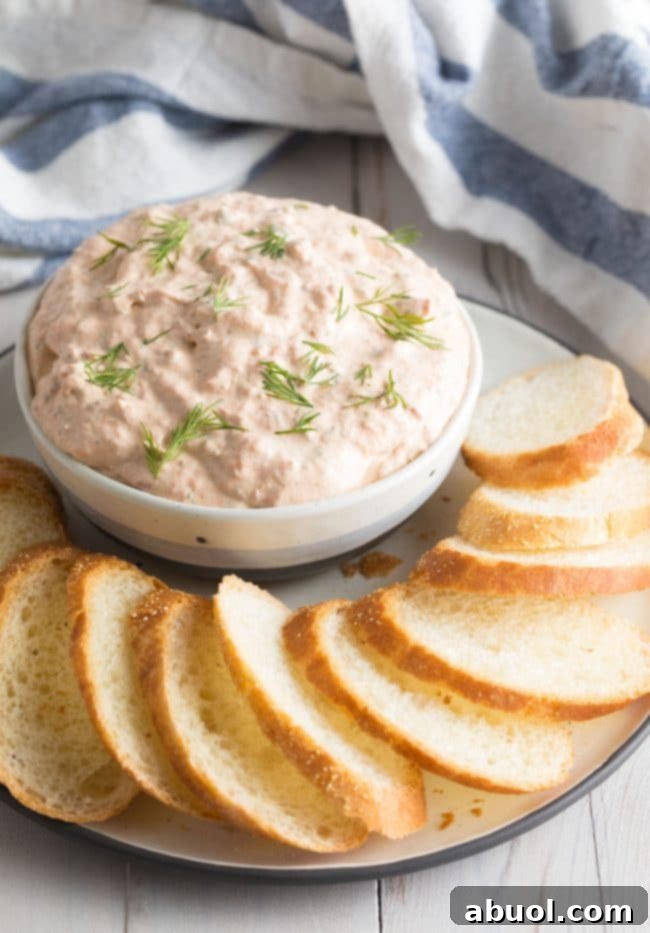 Creamy Smoked Salmon Dip 3 Small bowl filled with the smoked salmon dip, surrounded by toasted bread and fresh herbs on a plate.