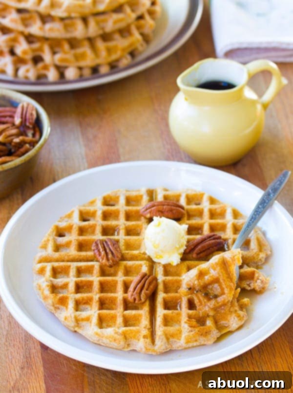 Healthy Spelt Waffles stacked on a plate with fresh fruit and syrup, a nutritious start to the day.