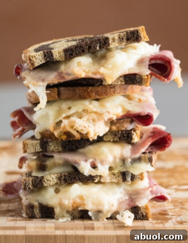 Reuben sandwiches stacked on top of each other. Golden brown bread, melted cheese, and hearty fillings are visible.