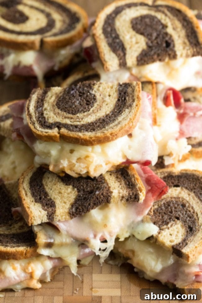 Baked Reuben sandwich recipe stacked on top of each other on a wooden background. The sandwiches are golden brown with melted cheese oozing out.