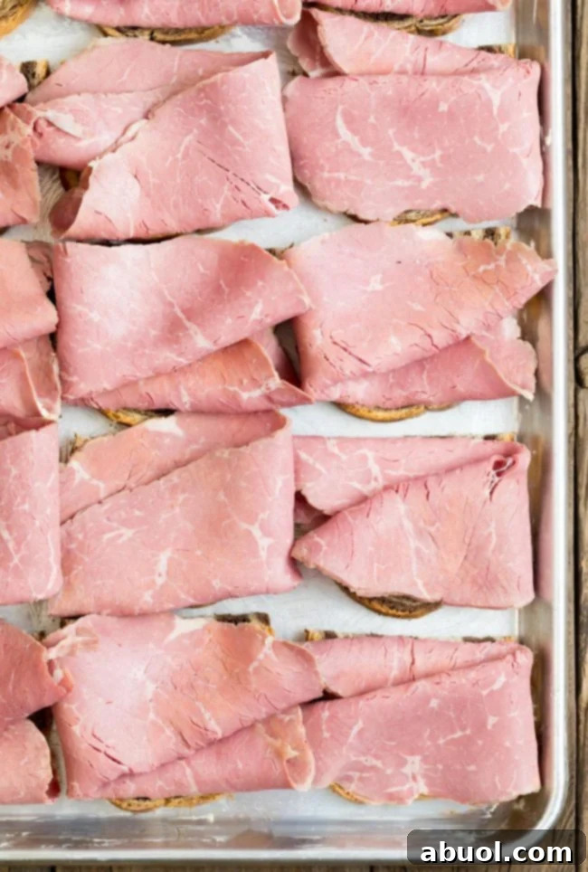 Bread assembled with corned beef slices on a sheet pan. Layers are starting to form on the bread.