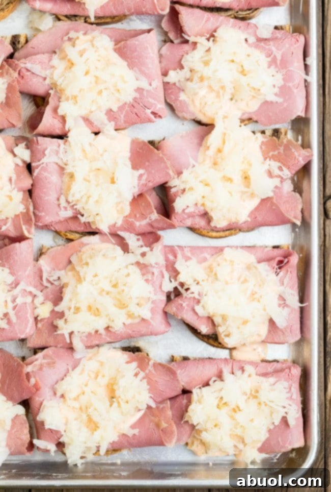 Bread topped with corned beef and sauerkraut on a sheet pan. The layers are neatly arranged.