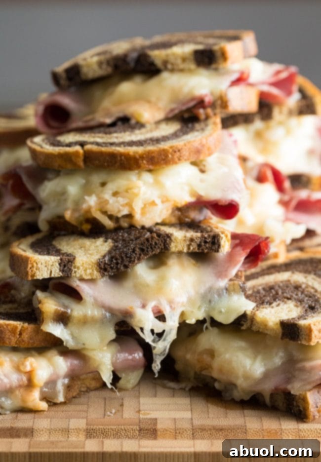 Reuben sandwiches piled on top of each other. The golden sandwiches are perfectly toasted and inviting.