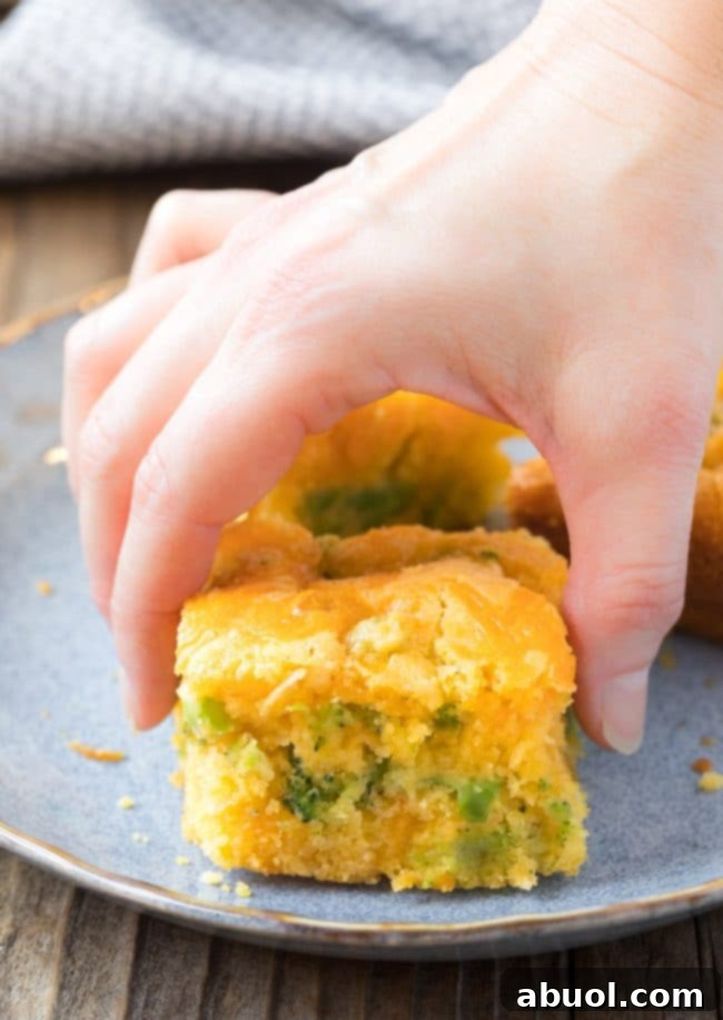 A hand picking up a piece of Jiffy broccoli cornbread from a baking pan, showing its soft interior and the ease of serving.