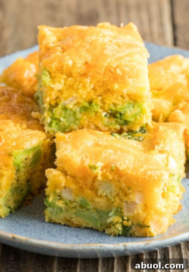 Close-up of a single slice of Jiffy broccoli cornbread on a white plate, showing visible pieces of broccoli and melted cheddar cheese for a hearty bite.