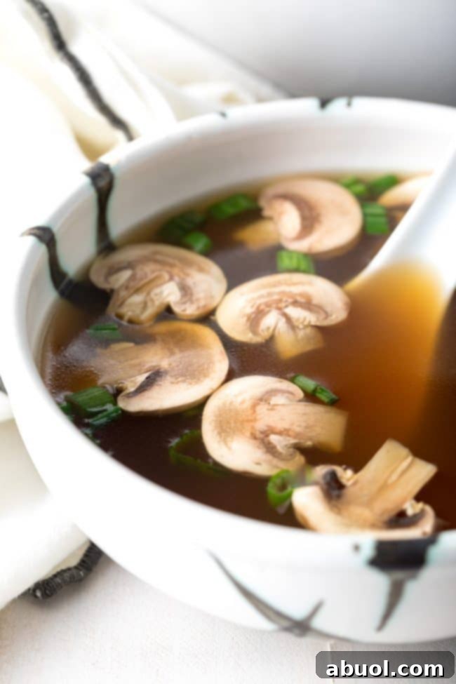 Bowl of healthy clear soup with mushrooms and scallions and a large soup spoon.