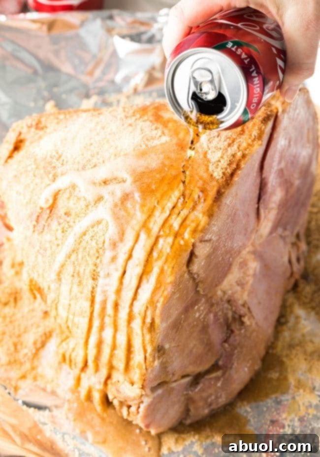 A hand pouring a can of Coca-Cola over a ham in a roasting pan before baking.