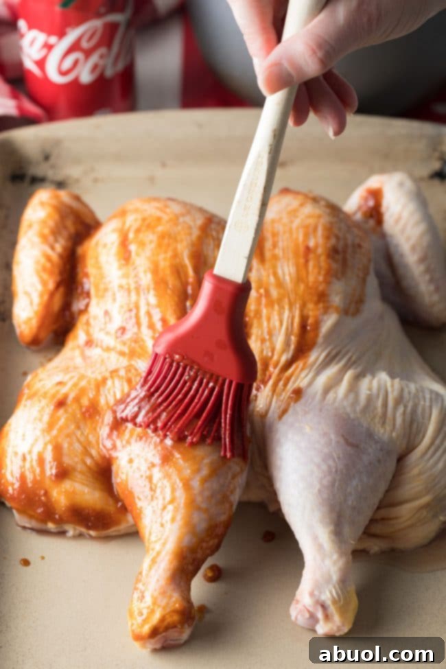 Spreading coca cola sauce across a spatchcock chicken before roasting.