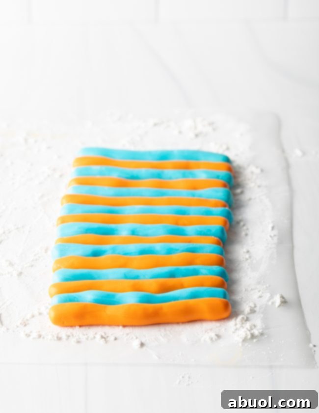 Homemade Fondant Magic 9 Orange and blue striped fondant being gently folded and prepped to be rolled out, showing a marbled effect.