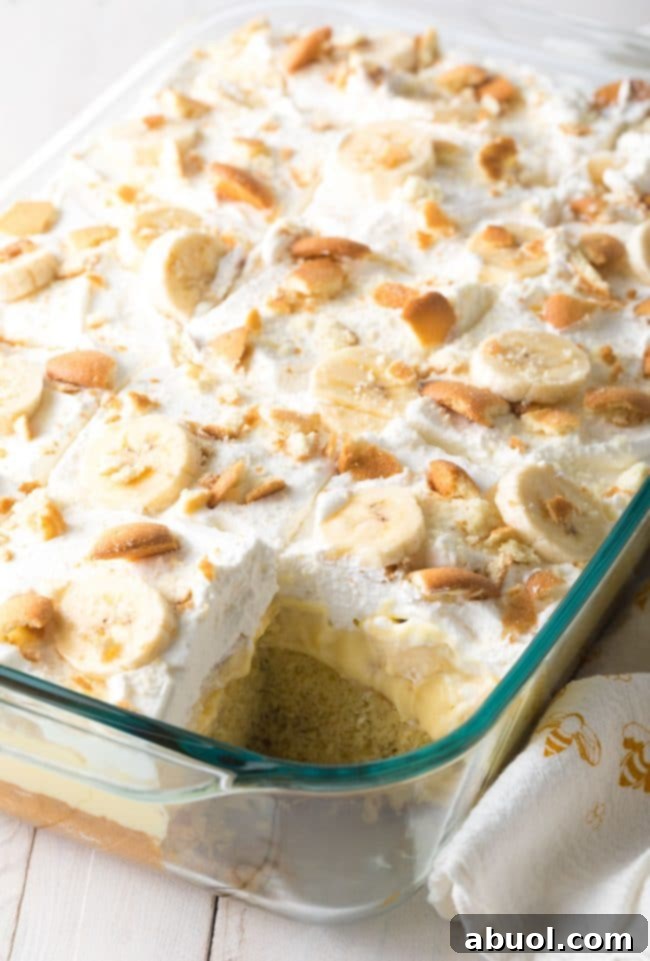 Decadent Banana Pudding Cake 3 Layered banana cake in a glass baking dish with a piece missing.