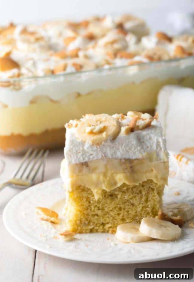 Decadent Banana Pudding Cake 4 Slice of banana pudding cake on a white plate with more cake in the background.