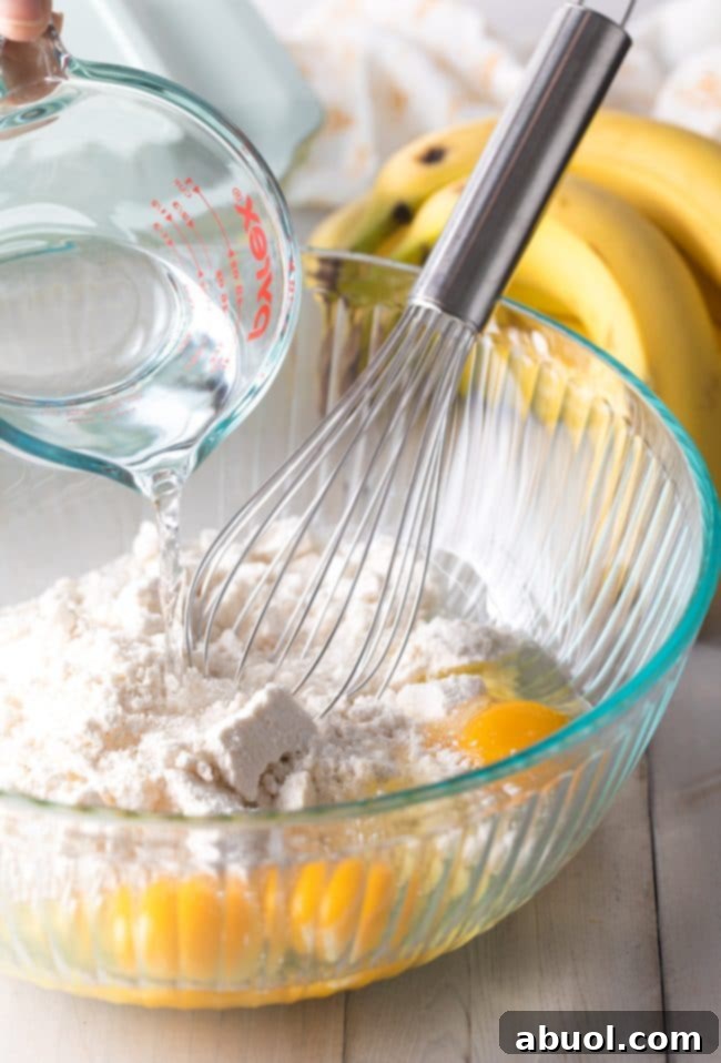 Decadent Banana Pudding Cake 5 Cake batter being whisked together in a glass mixing bowl.
