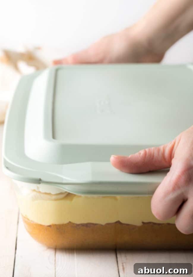 Decadent Banana Pudding Cake 10 Pyrex Deep Dish with hands putting a lid on top to store.